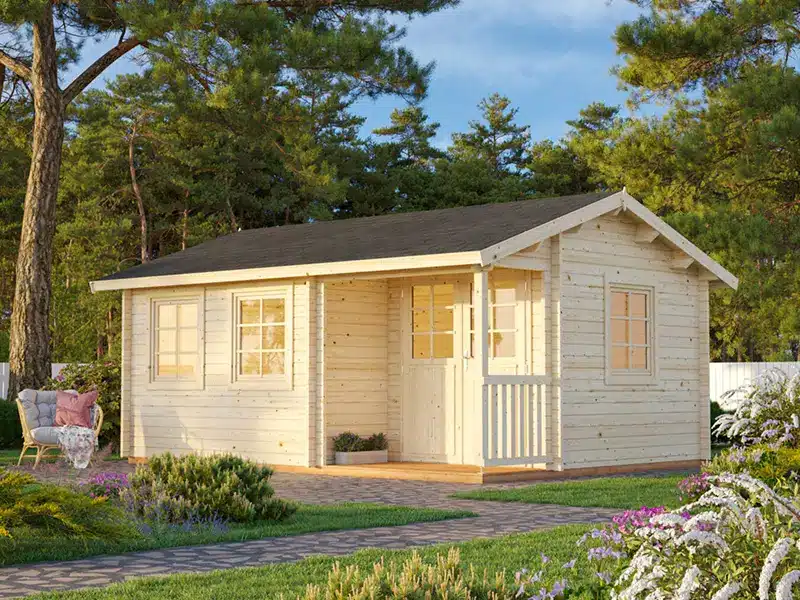 Petit chalet en bois clair avec terrasse et volets, installé dans un jardin verdoyant entouré d’arbres.