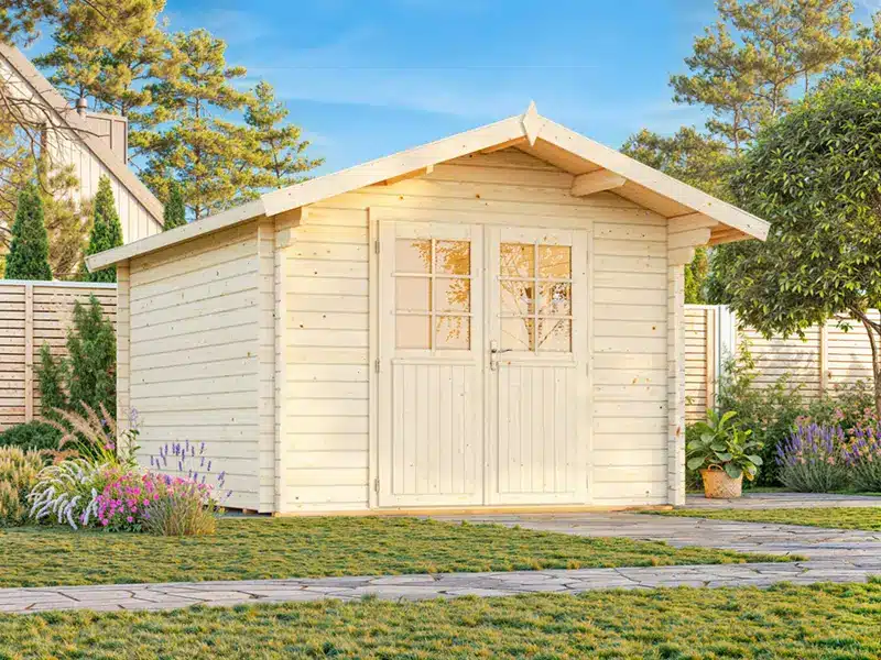 Cabane de jardin en bois clair avec portes doubles, installée dans un jardin ensoleillé entouré d’arbres et de fleurs.