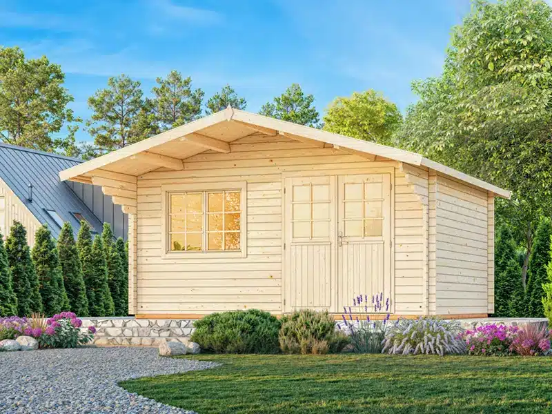 Abri de jardin en bois à toit en pente, avec porte double et fenêtre, entouré de buis et de fleurs sur une pelouse verdoyante.