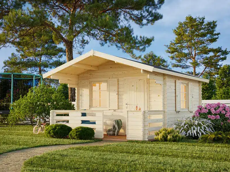 Petit chalet en bois pour jardin avec terrasse, entouré d’un jardin verdoyant et d’arbres.