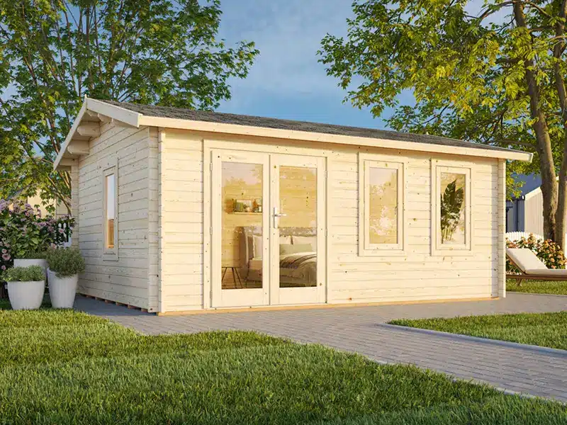 Abris de jardin en bois clair avec de grandes fenêtres et des portes vitrées, installé sur une allée entourée de pelouse et d’arbres.