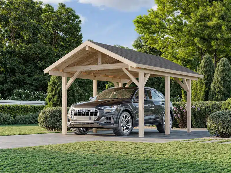 Carport en bois avec toit en pente abritant une voiture dans un jardin verdoyant.