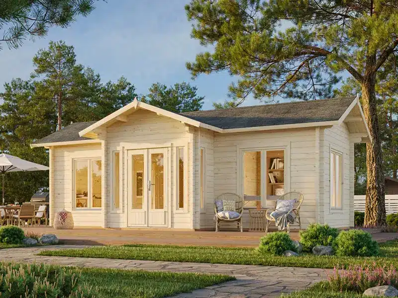Chalet de jardin en bois clair avec de grandes portes vitrées et une terrasse, entouré d’arbres.