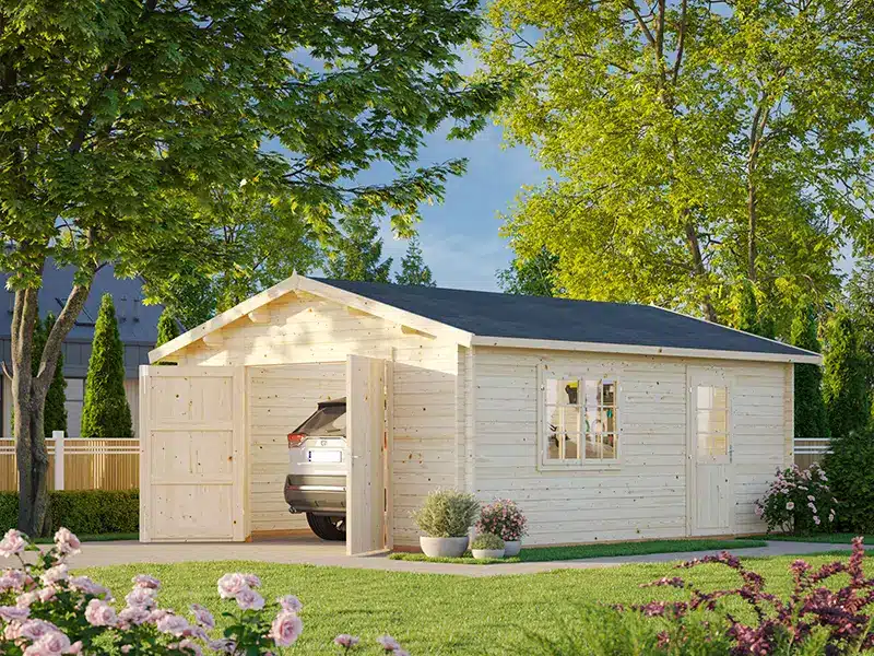 Abri de jardin en bois blanc avec garage intégré et voiture garée, entouré d’un jardin verdoyant et d’arbres.