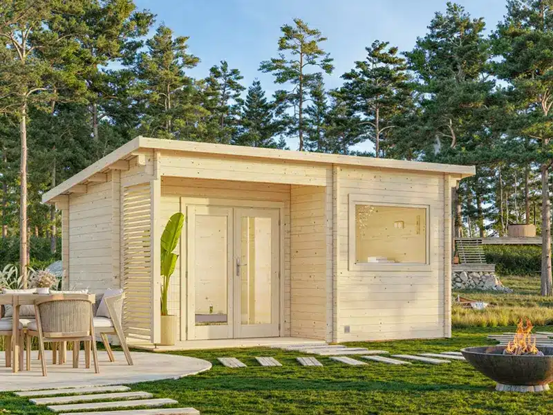 Abris de jardin en bois et petit chalet sur terrasse en bois, avec porte et fenêtres vitrées, mobilier extérieur et arbres en arrière-plan.