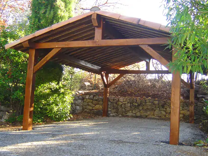 Pavillon de jardin en bois à toit en pente, structure ouverte sur quatre poteaux, installé sur un espace extérieur près d'un mur en pierre.
